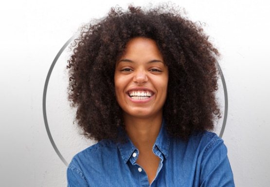 Smiling young woman with curly hair, wearing a blue shirt, happy after Canesten thrush treatment